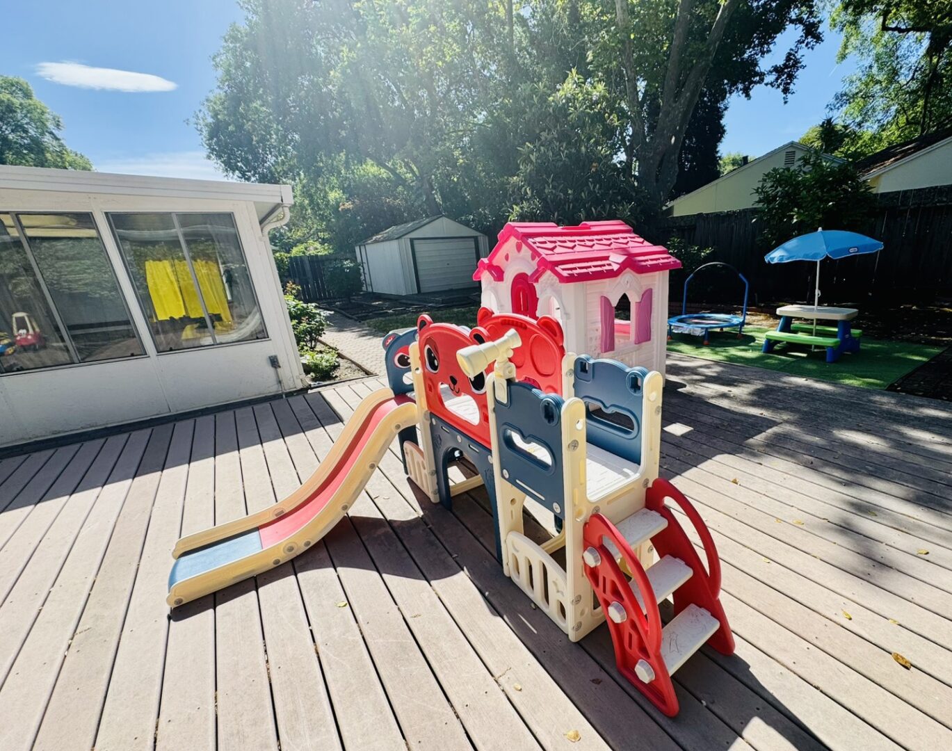 Children's outdoor playset with slide and playhouse on a sunny deck.