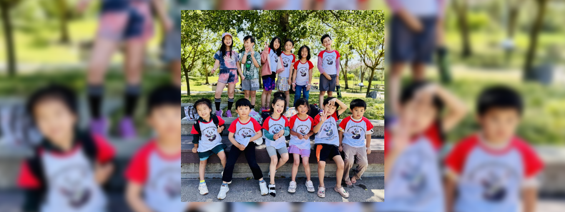 Group of children and adults posing happily outdoors in matching shirts.
